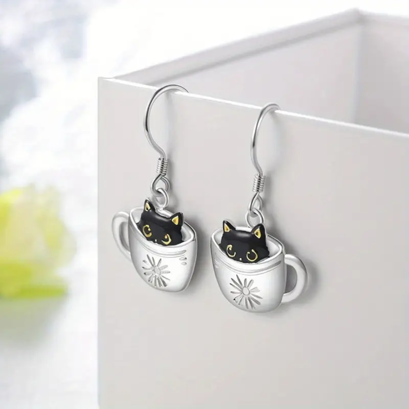 Cat-themed earrings with black cats inside silver mugs on a white background