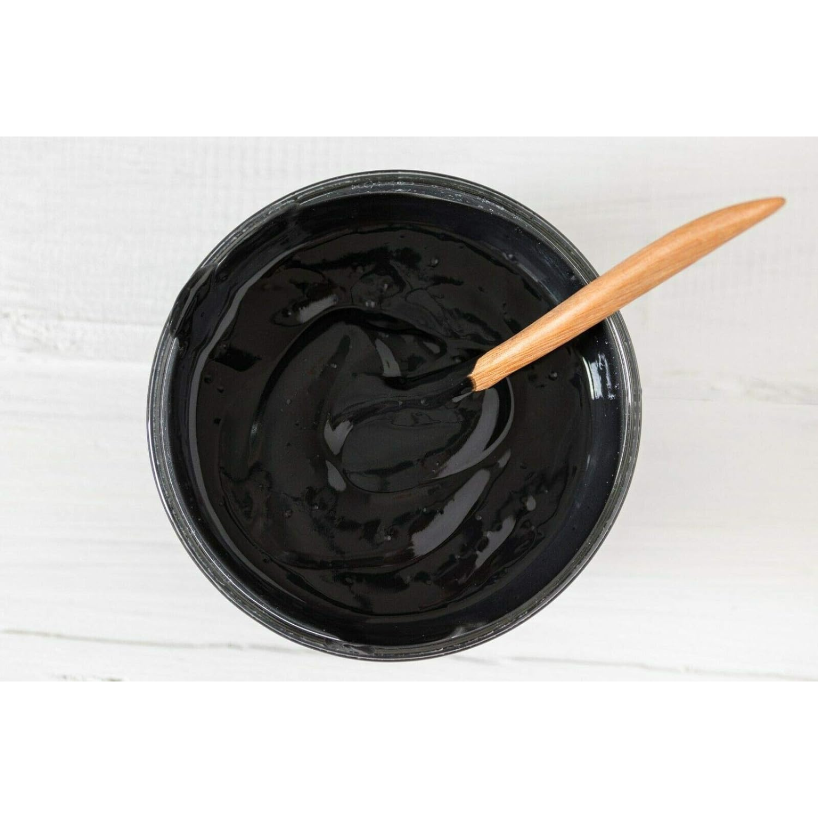 Black hair dye in a bowl with a wooden spoon on a white background