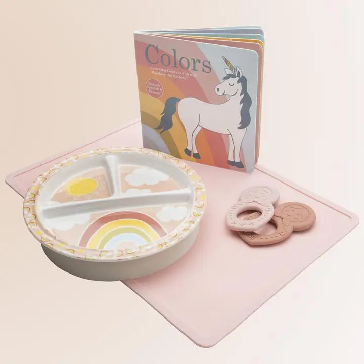 Children's plate with rainbow design, coloring book with unicorn, and cookies on a pink surface