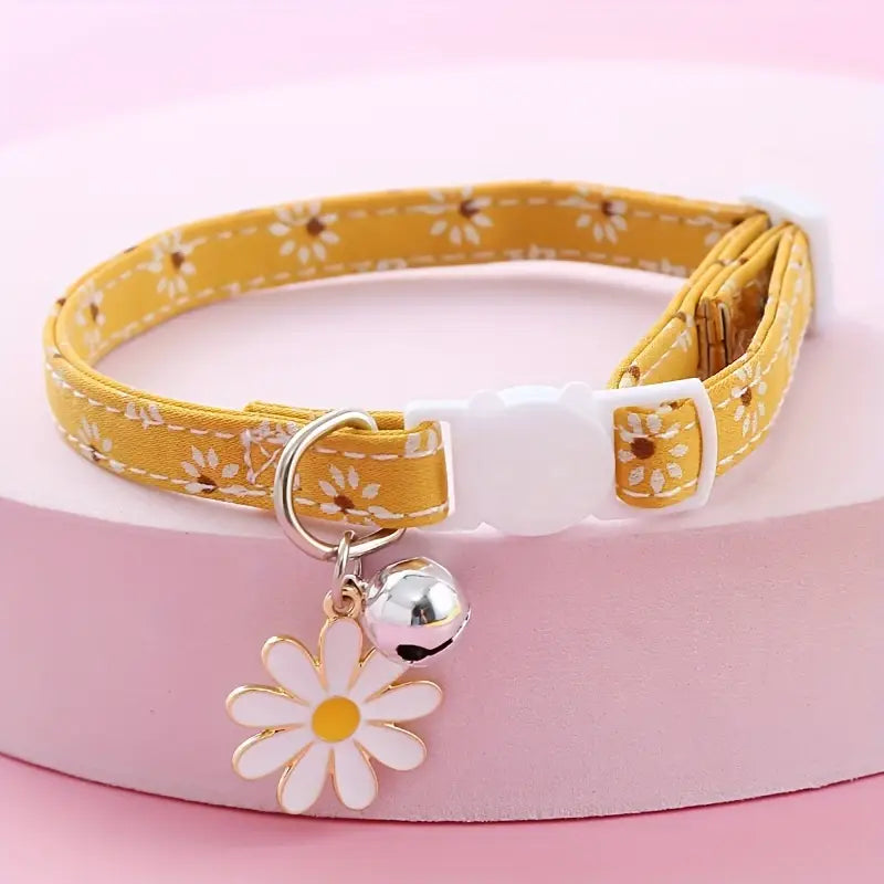 Yellow floral-patterned pet collar with a white flower charm and bell on a pink background