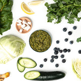 Assorted fresh vegetables and a bowl of green pesto on a white background