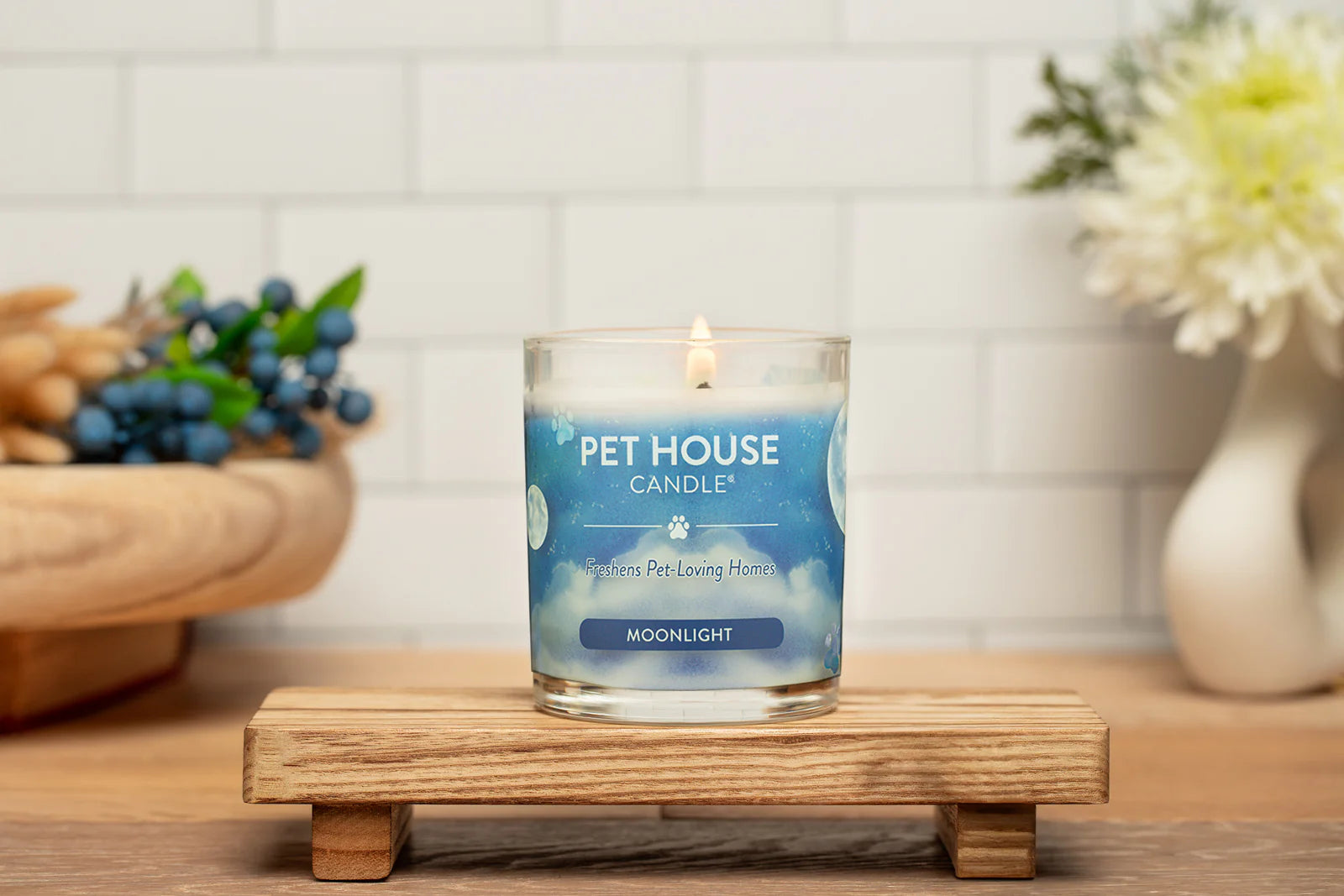Pet House Candle on a wooden stand with a white tiled wall and decorative elements in the background