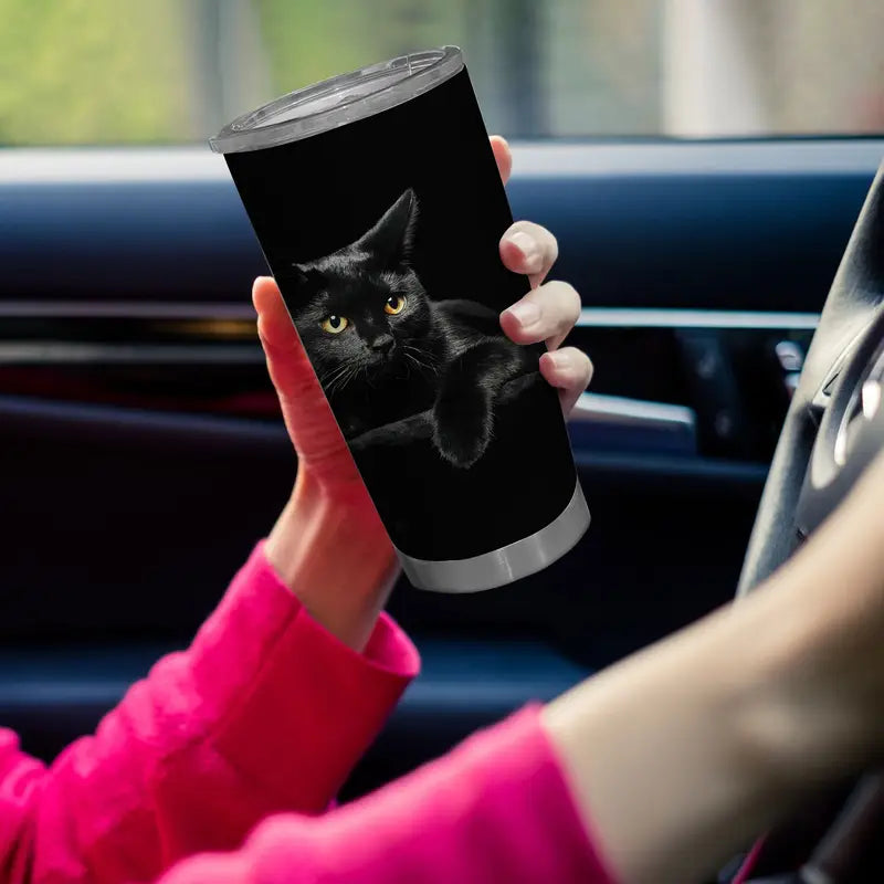 Person holding a black tumbler with a cat design inside a car.