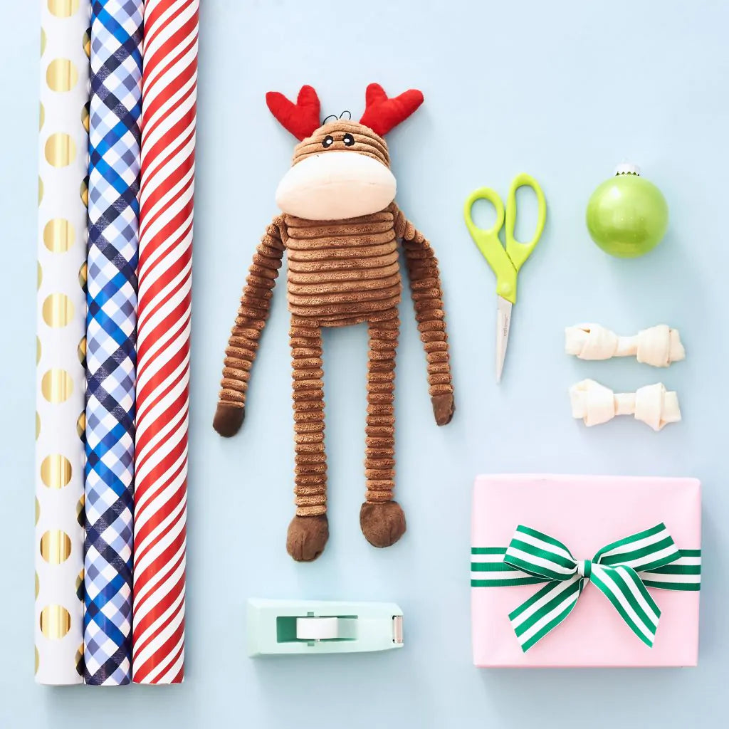 Decorative items including a plush reindeer, gift wrap, scissors, and a present on a light blue background.