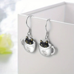 Cat-themed earrings with black cats inside silver mugs on a white background