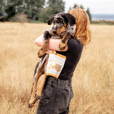 Person holding a dog in a field with a product packaging visible
