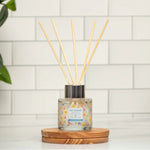 Diffuser with sticks on a wooden coaster against a tiled wall.