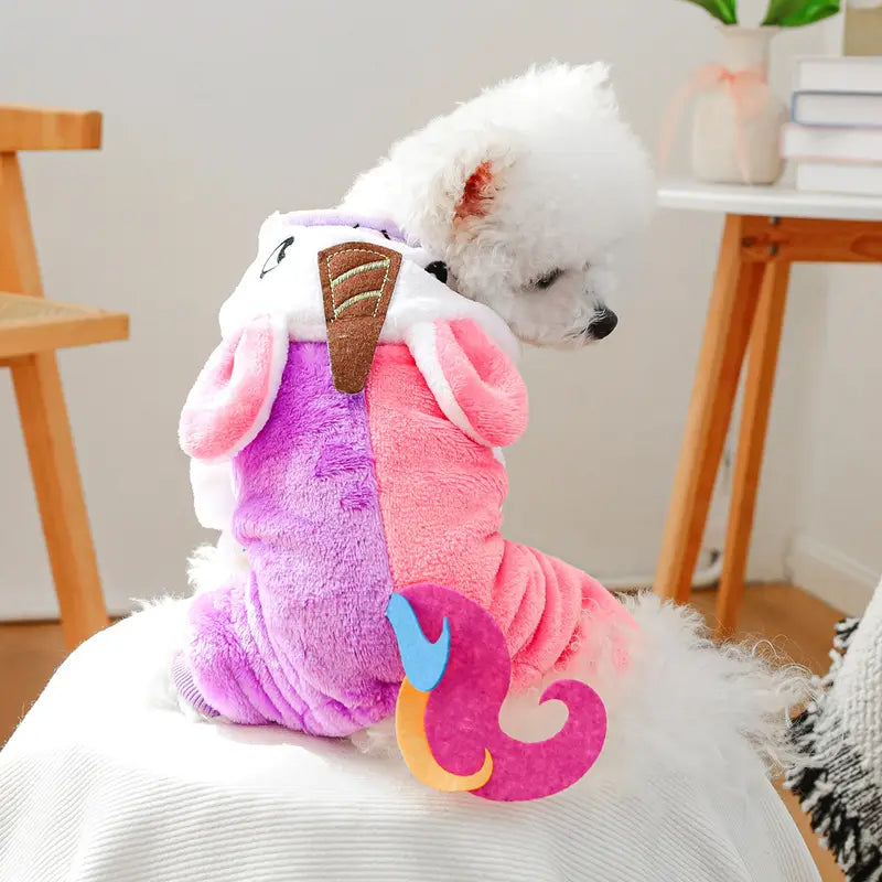 Small dog wearing a colorful unicorn costume sitting on a white surface.
