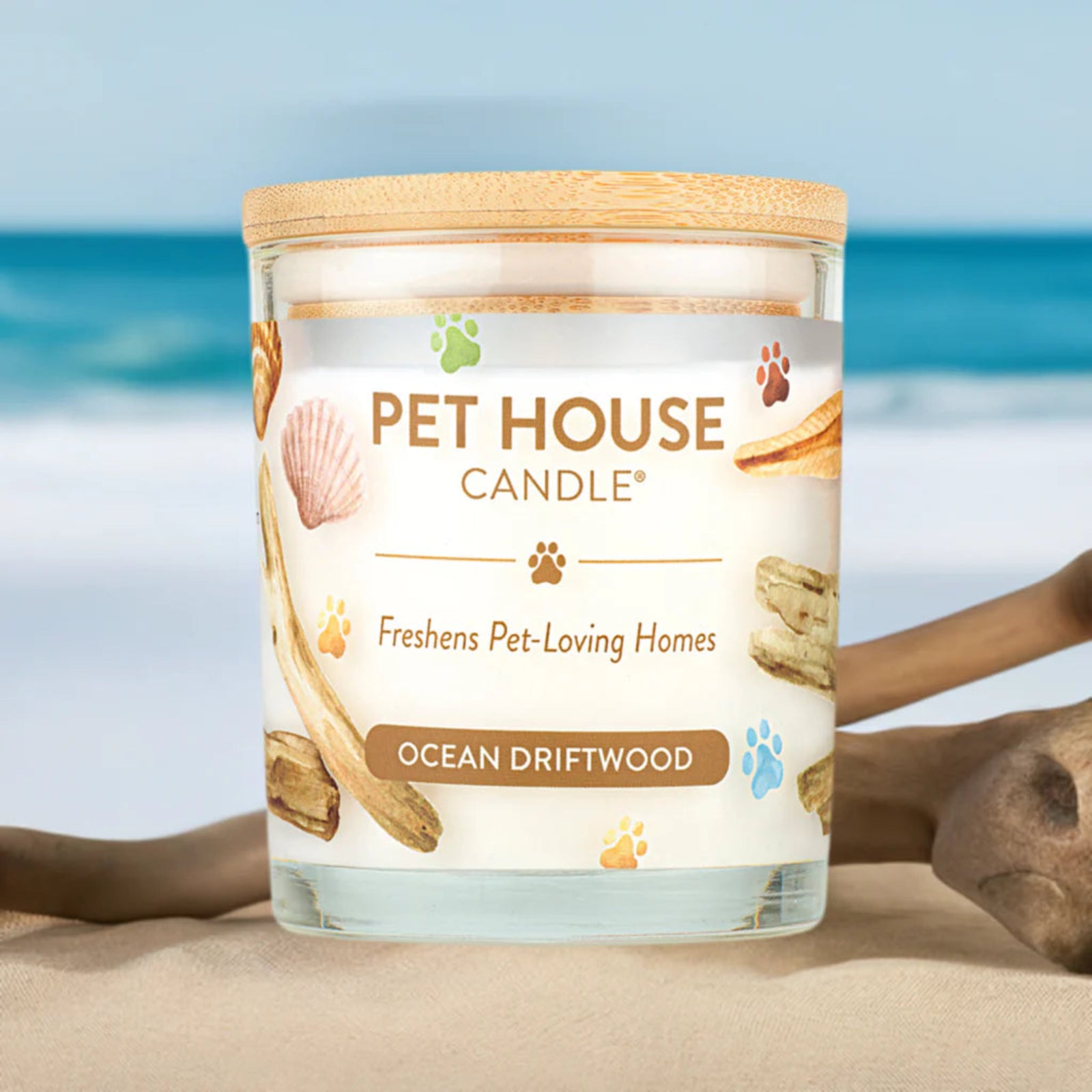 Pet House Candle labeled 'Ocean Driftwood' on a beach with ocean in the background