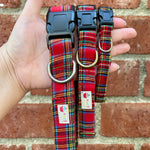 Red plaid dog collars with a brand label held against a brick wall.