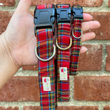 Red plaid dog collars with a brand label held against a brick wall.