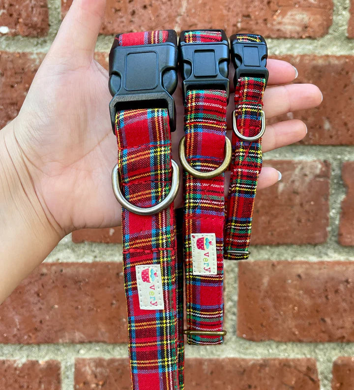Red plaid dog collars with a brand label held against a brick wall.