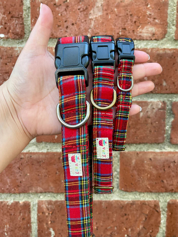 Red plaid dog collars with a brand label held against a brick wall.